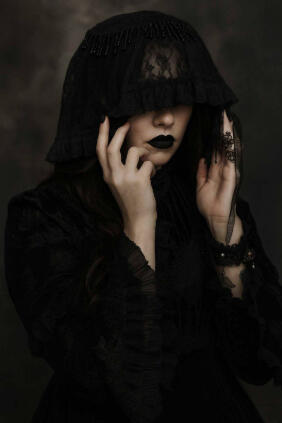 Rowan Author Photo Photo of Rowan in black lace veil, partially covering her face with both hands, gothic and mysterious expression.